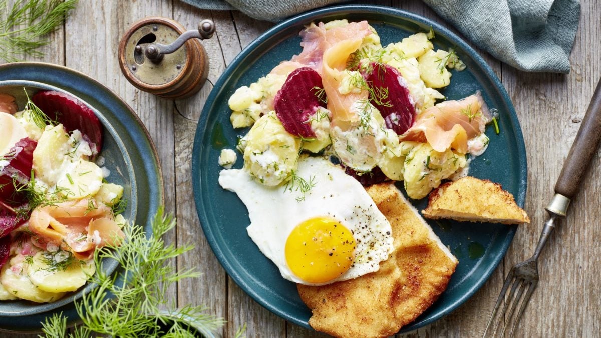 Kapitäns-Schnitzel mit Spiegelei auf einem blauen Teller auf hölzernem Hintergrund. Daraus Dill, eine Pfeffermühle und eine Gabel.