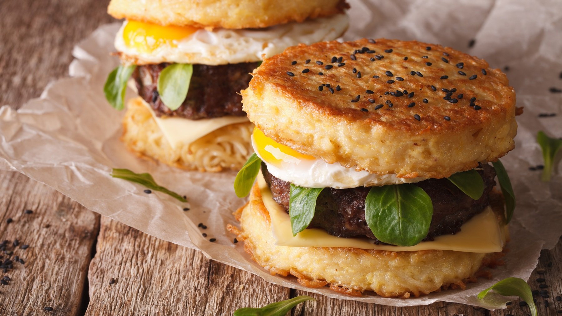 Zwei Blumenkohl-Burger auf einem dunklen Holztisch mit hellem Backpapier.